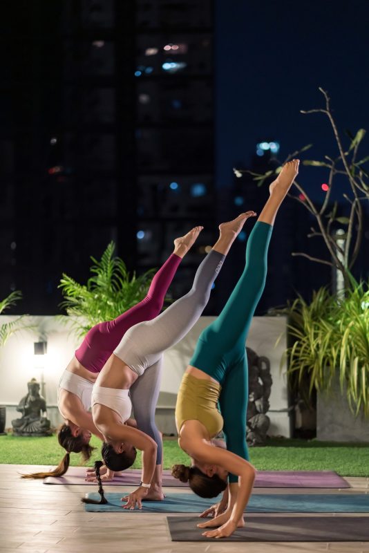 Asian weman group do yoga in city at night Group of asian women in sportswear pants practicing yoga during city lockdown in their apratment with distance in background of cityscape illumination night. Work out fitness healthy lifestyle concept
